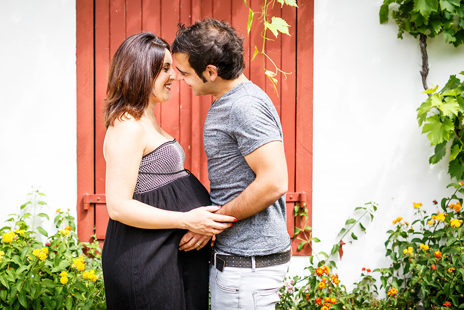 pareja besándose en una puerta roja en un reportaje de embarazo