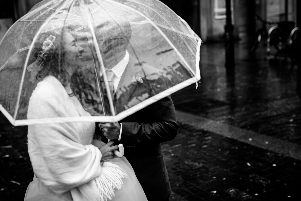 pareja de novios debajo de un paraguas transparente en un reportaje de boda en donostia