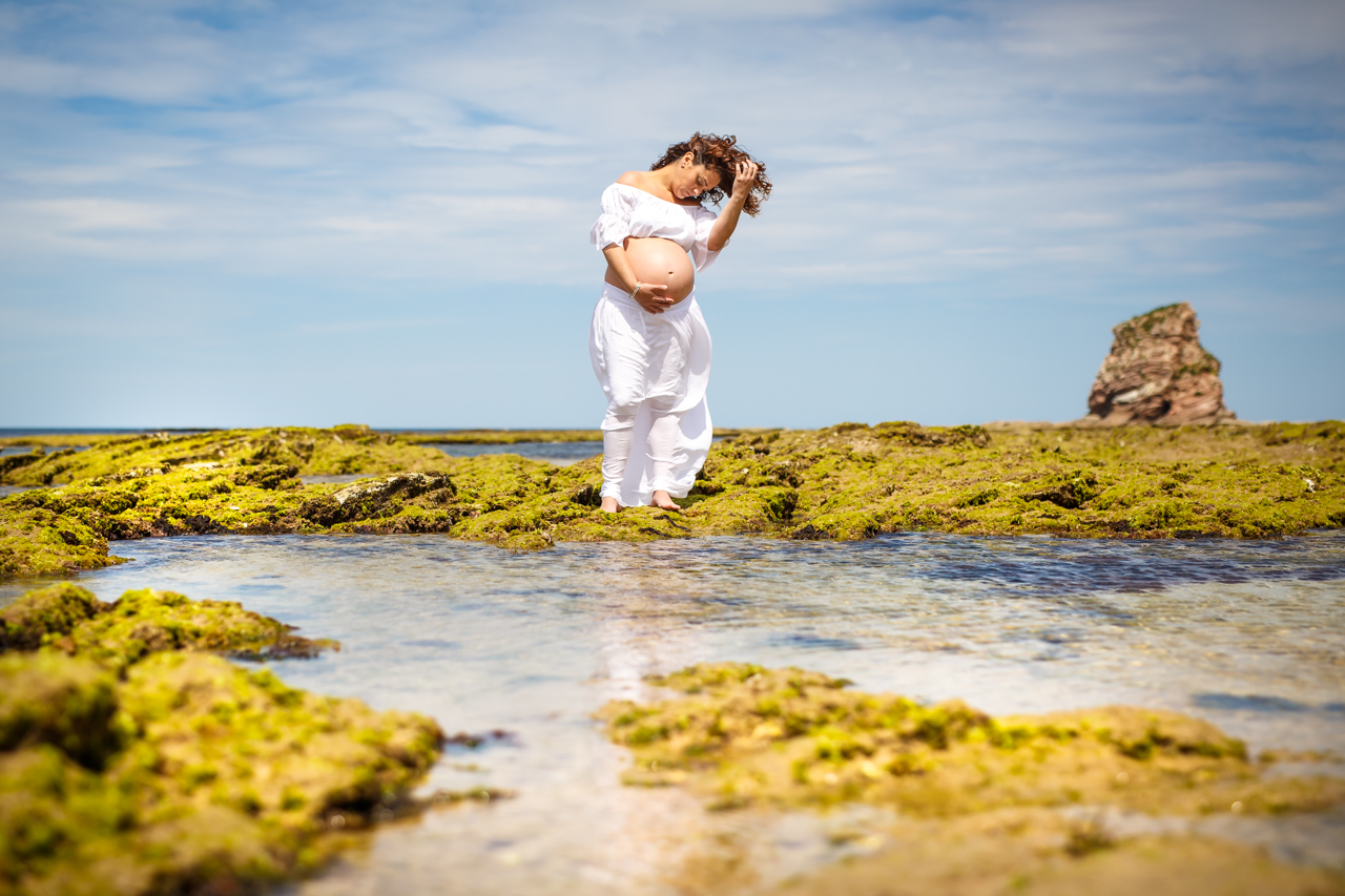 embarazada en la playa agarrándose el pelo en el agua